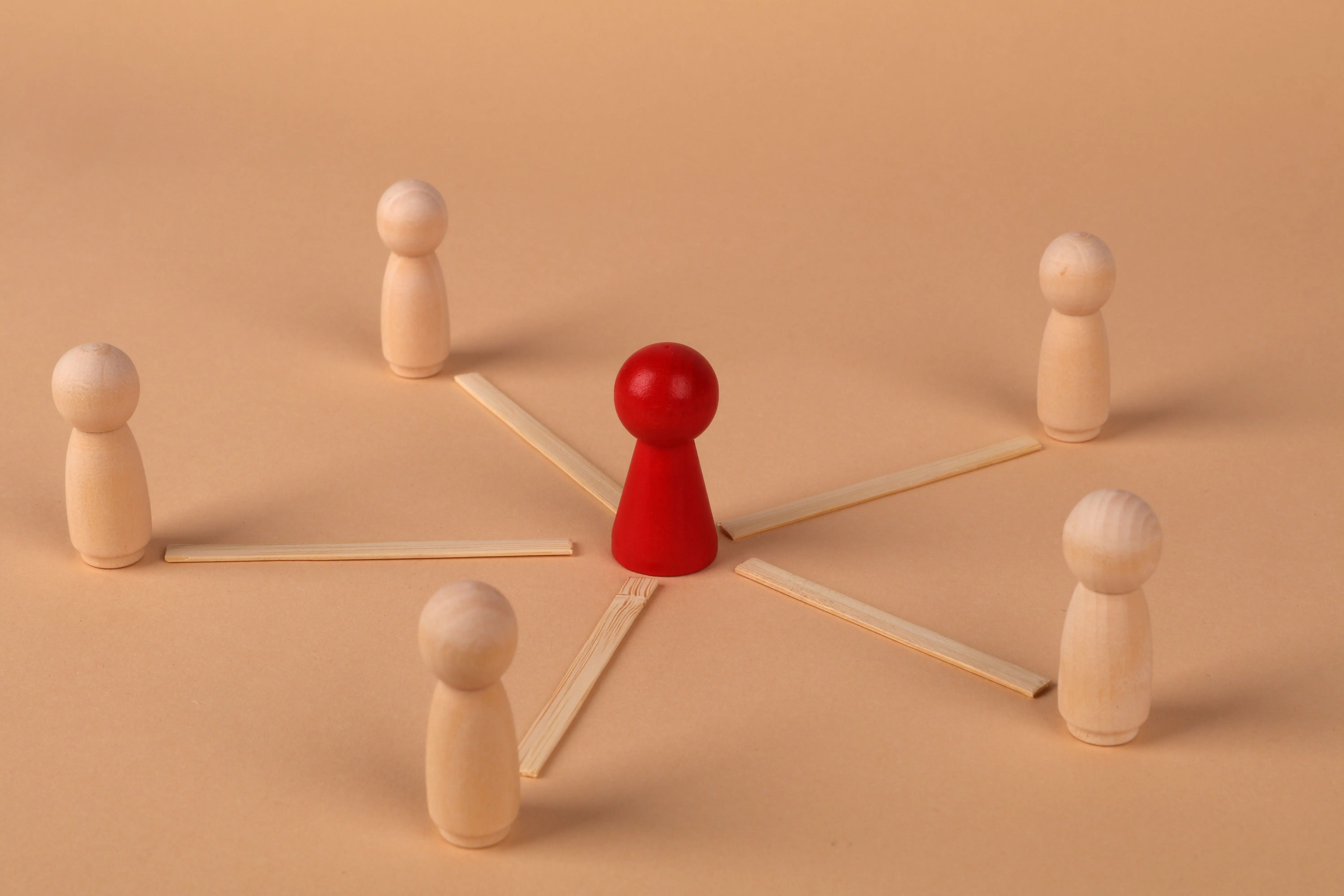 Wooden figures with red leader representing teamwork and influence