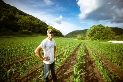 A farmer standing thoughtfully in a lush garden environment during daytime