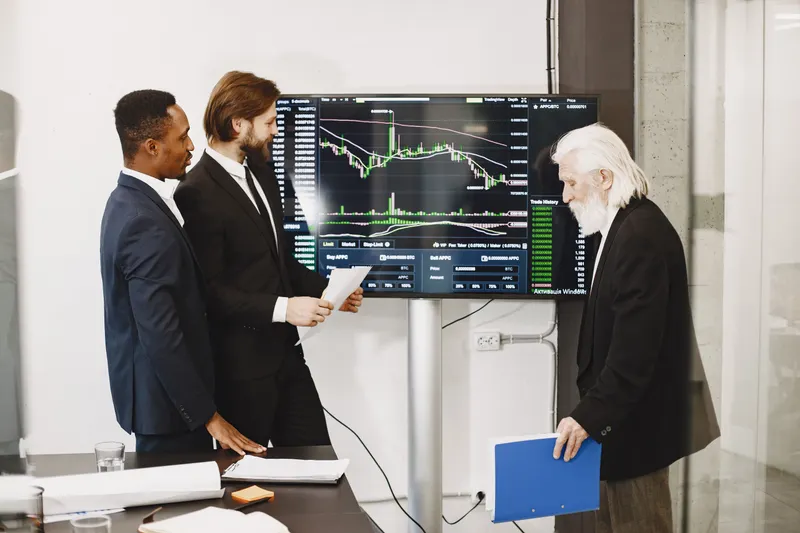 Three analysts reviewing financial charts on a shared screen