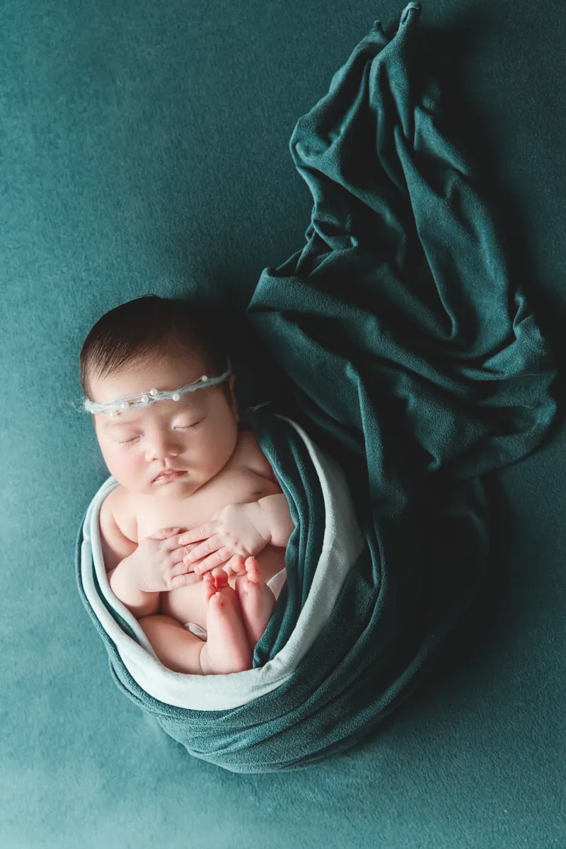 Newborn baby peacefully sleeping wrapped in a soft teal fabric